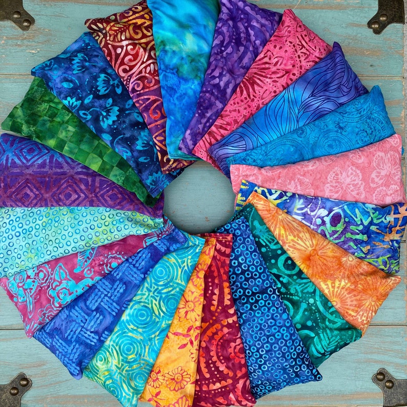May include: A collection of 18 colorful fabric-covered eye pillows arranged in a circle. The pillows are made of different fabrics with various patterns and colors, including blue, green, purple, pink, and orange.