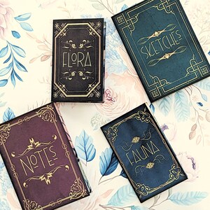 May include: Four small, decorative notebooks with gold lettering and ornate designs. The notebooks are titled "Flora", "Fauna", "Notes", and "Sketches".