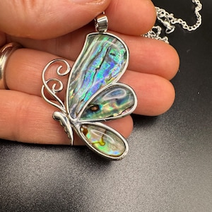 May include: A butterfly pendant necklace with iridescent abalone shell wings and a silver-tone metal frame. The pendant is suspended from a delicate silver chain. The butterfly design features intricate details and a polished finish.