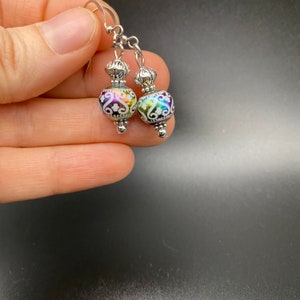 May include: A pair of silver dangle earrings with iridescent glass beads. The beads are decorated with a white floral pattern.