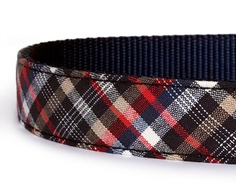 May include: Close-up of a dog collar with a plaid pattern in red, black, white, and tan. The collar's interior is a solid navy blue. The fabric is tightly woven, suggesting durability.