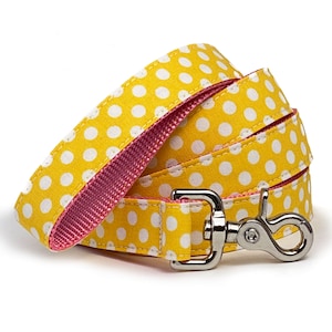 May include: A yellow dog lead with white polka dots and a pink lining. The lead has a silver metal clip.