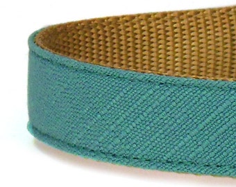 Puede incluir: Un collar para perro azul turquesa con forro de cinta marrón. El collar está hecho de una tela suave y texturizada.