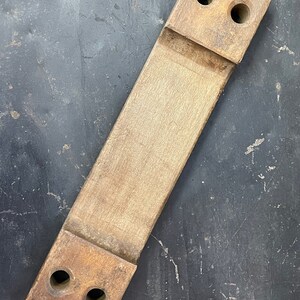 May include: A wooden block with two holes on each end. The block is light brown and has a smooth surface.