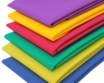May include: A stack of six folded fabric pieces in solid colors, arranged from top to bottom in purple, yellow, pink, green, light yellow, and blue. Each piece of fabric is neatly folded into a rectangular shape with visible woven texture.