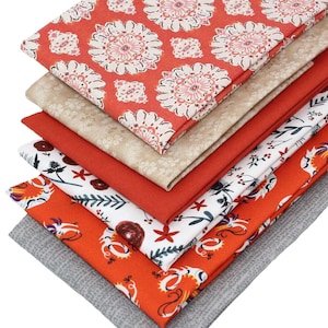 May include: A selection of folded fabric squares in various patterns and colours. The fabrics feature floral, botanical, and geometric designs in shades of red, orange, beige, white, and grey. The fabrics are likely cotton or a similar material.
