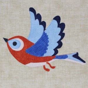 Può includere: Un uccello blu e rosso con un occhio bianco, che vola con le ali spiegate. L'uccello è fatto di stoffa e ha un design cucito.