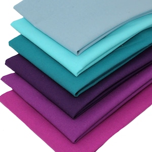 May include: A collection of six fabric squares in a gradient of colours, from light blue to deep magenta. The shades include teal and purple. Each square is neatly folded, displaying the fabric's texture and colour variations. The image suggests a craft or textile theme.