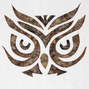 Könnte beinhalten: Ein braunes und goldenes Eulenkopfdesign mit aufwendigen Stickdetails. Die Augen der Eule sind schwarz umrandet und der Schnabel ist goldgelb.