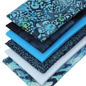 May include: A stack of six fabric squares in shades of blue and green with a variety of patterns. The fabric is soft and has a subtle sheen.