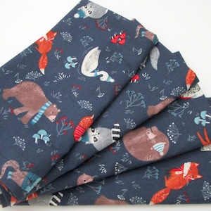 May include: Folded navy blue fabric featuring a whimsical forest animal print. The design includes foxes, bears, raccoons, and swans, all adorned with scarves and hats. The fabric is decorated with floral and mushroom elements.