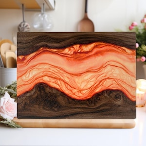 以下が含まれることがあります： ユニークなデザインの長方形まな板。濃い茶色の縁と、中央に鮮やかなオレンジと赤の波模様があります。まな板は、キッチンでの使用に適した、明るい茶色の木製の台座の上に置かれています。長さは約30cmです。