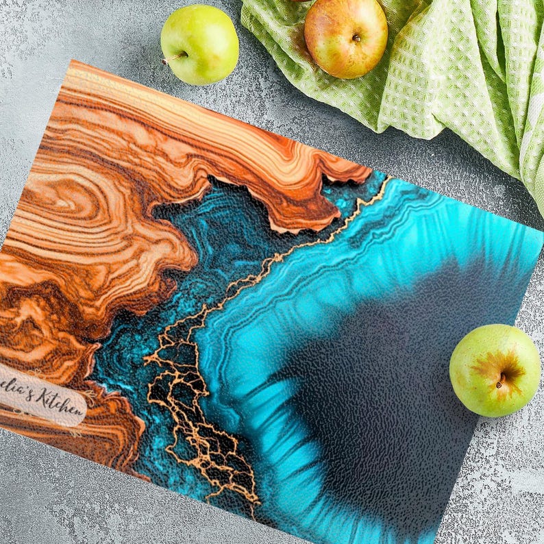 May include: A rectangular wooden cutting board with a blue and gold epoxy resin inlay. The board has a natural wood grain pattern and is signed "Julia's Kitchen".
