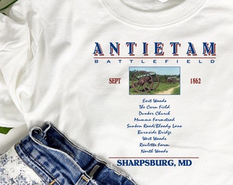 May include: White t-shirt with a graphic design of the Antietam Battlefield. The graphic includes a cannon, trees, and the text "Antietam Battlefield", "Sept", "1862", and "Sharpsburg, MD".