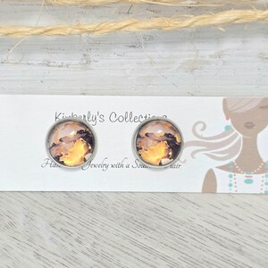 May include: A pair of earrings with a silver setting and a round, colorful, abstract design. The earrings are displayed on a white card with the text "Kimberly's Collection Handmade Jewelry with a Soulful Flair".