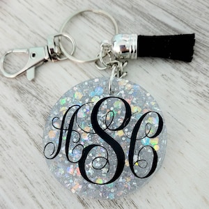 May include: A silver keychain with a black tassel and a round, clear, glitter-filled charm with a black monogram "HSC".