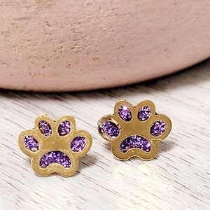 May include: A pair of gold-tone stud earrings with a purple glitter paw print design.