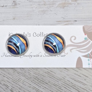 May include: A pair of silver stud earrings with blue, black, and gold abstract designs. The earrings are on a white card with the text "Kimberly's Collection Handmade Jewelry with a Southern Flair".
