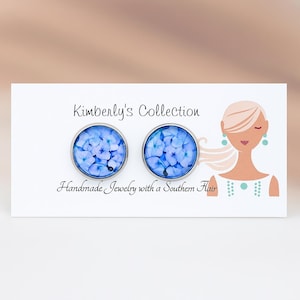 May include: A pair of round, silver-toned stud earrings. Each earring features a blue floral design. The card reads "Kimberly's Collection" and "Handmade Jewelry with a Southern Flair."