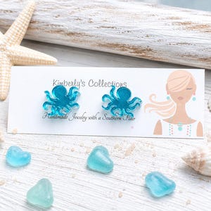 May include: Turquoise octopus stud earrings on a white card with the text "Kimberly's Collections Handmade Jewelry with a Southern Hair". The earrings are displayed with seashells and blue heart-shaped glass pieces.