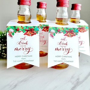 May include: Five miniature bottles of liquor with festive Christmas gift tags. The tags feature a watercolor design of holly, bells, and a stocking. The text on the tags reads "eat, drink, and be merry" with a Merry Christmas greeting from The Happy Company.