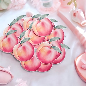 May include: A collection of peach-colored paper peach cutouts with green leaves. The peaches are arranged in a circular pattern with the leaves overlapping.