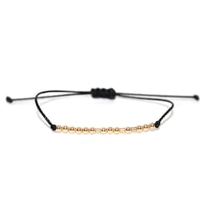 May include: A simple gold bead bracelet with a black cord. The bracelet is adjustable and can be worn on any wrist size.