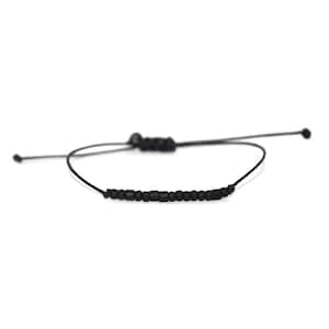 May include: A black beaded bracelet with a black cord and adjustable sliding knot closure.