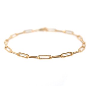 May include: A gold chain bracelet with a simple, linked design. The chain is made of small, oval-shaped links.