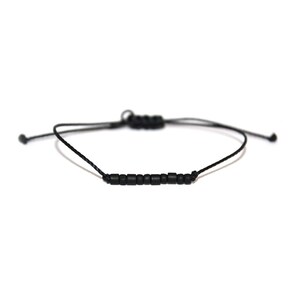May include: A black beaded bracelet with a black cord and adjustable sliding knot closure.