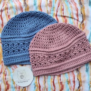 Puede incluir: Dos gorros de ganchillo hechos a mano en azul y rosa empolvado. Los gorros tienen un patr&oacute;n de puntada texturizada y se muestran sobre una tela estampada colorida. Tambi&eacute;n hay un peque&ntilde;o posavasos redondo con una ilustraci&oacute;n de b&uacute;ho y el texto "The Funky Purple Owl".