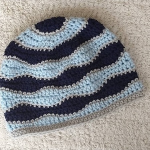 May include: A crocheted hat with a wavy pattern in blue, gray, and black.