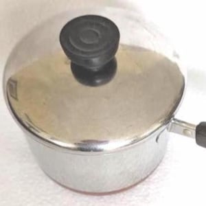 May include: A small stainless steel saucepan with a polished silver finish, featuring a matching lid with a black circular knob and a long, black heat-resistant handle extending from the side for easy gripping and maneuverability.