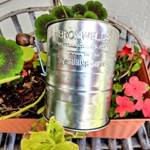 May include: Silver measuring sifter with a crank handle. The sifter is labeled "Bromwell's Michigan City, Ind. 46360 Made in USA Measuring Sifter".