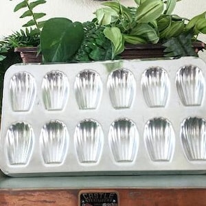 May include: A silver metal baking pan with 12 individual molds shaped like seashells. The pan is labeled "CASTLE STERILIZER"