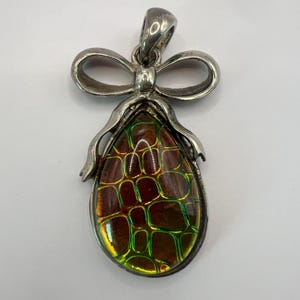 May include: A silver pendant with a teardrop-shaped iridescent green and brown stone set in a silver bow.