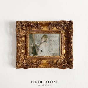 May include: A gold framed painting of a woman in a white dress, standing in front of a mirror. The painting is set against a white wall.