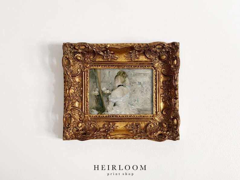 May include: A gold framed painting of a woman in a white dress, standing in front of a mirror. The painting is set against a white wall.