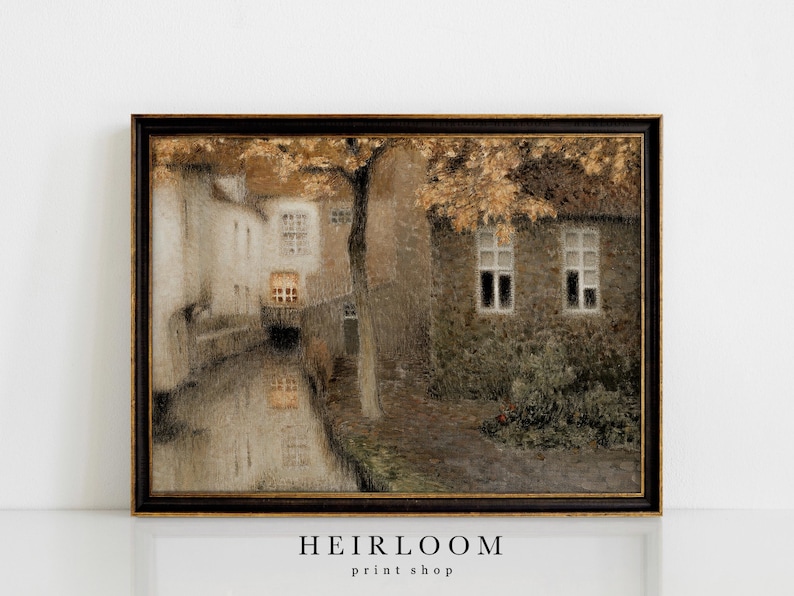 May include: Framed vintage print of a European canal scene. The artwork features buildings with windows, a tree with golden leaves, and a reflection in the water. The frame is dark with gold accents. The text "HEIRLOOM print shop" is at the bottom.