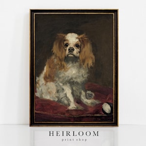 Könnte beinhalten: Gerahmtes Vintage-Porträt eines Cavalier King Charles Spaniel. Der Hund hat braunes und weißes Fell und sitzt auf einem roten Kissen. Das Kunstwerk ist vor einem dunklen Hintergrund. Der Rahmen ist schwarz und gold. Der Text "HEIRLOOM print shop" steht unten.
