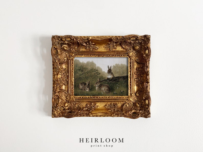 May include: A framed print featuring a pastoral scene with several rabbits in a forest setting. The artwork is enclosed in an ornate, gold-colored frame. The text "HEIRLOOM print shop" is at the bottom of the image.