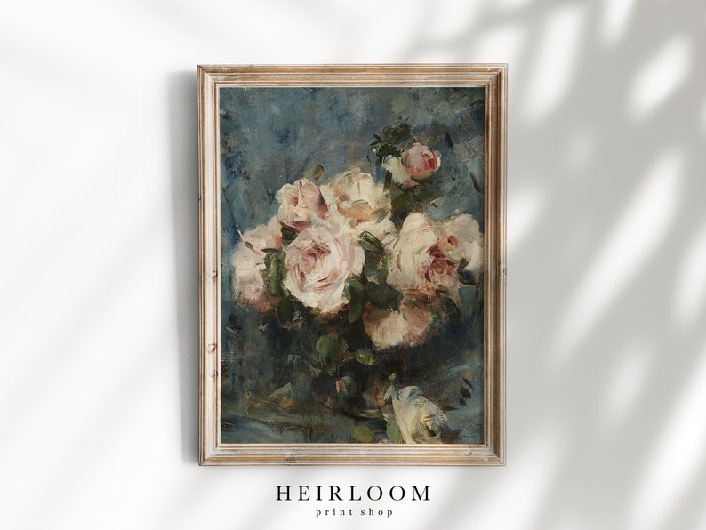 Op de afbeelding: Een ingelijst bloemenschilderij met een boeket witte en roze rozen tegen een blauwe achtergrond. Het kunstwerk heeft een vintage uitstraling met zichtbare penseelstreken en is geplaatst in een lichtgekleurde houten lijst. De tekst "HEIRLOOM print shop" staat onderaan.