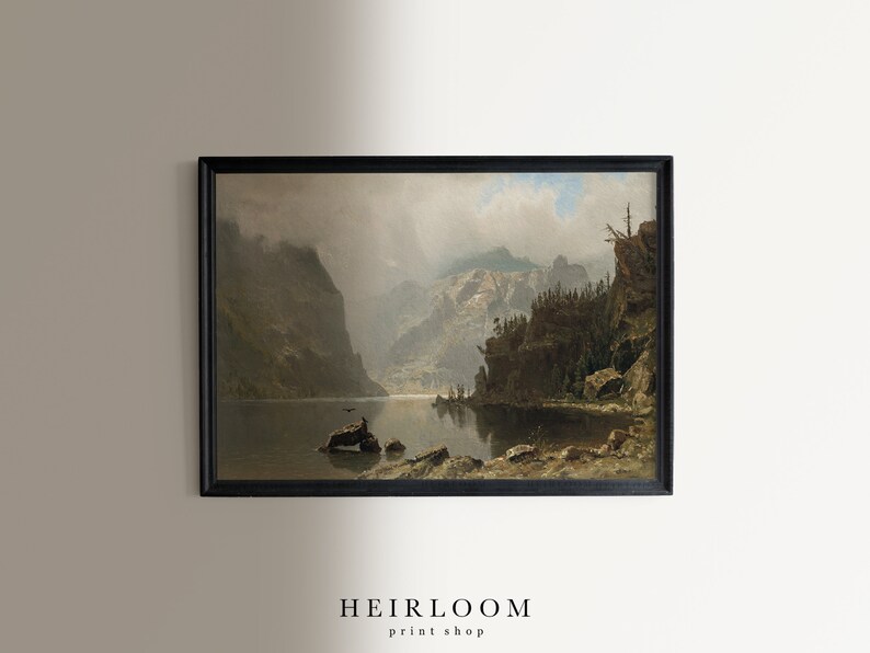 May include: Framed landscape art print featuring a serene lake scene surrounded by towering mountains. The artwork is in muted tones of gray, brown, and green, with a black frame. The text "HEIRLOOM print shop" is at the bottom.