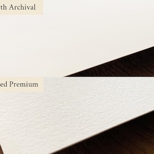 May include: A side-by-side comparison of two types of paper. The top section displays smooth, white paper labeled "Smooth Archival." The bottom section shows textured, off-white paper labeled "Textured Premium." The paper samples are on a dark wood surface.