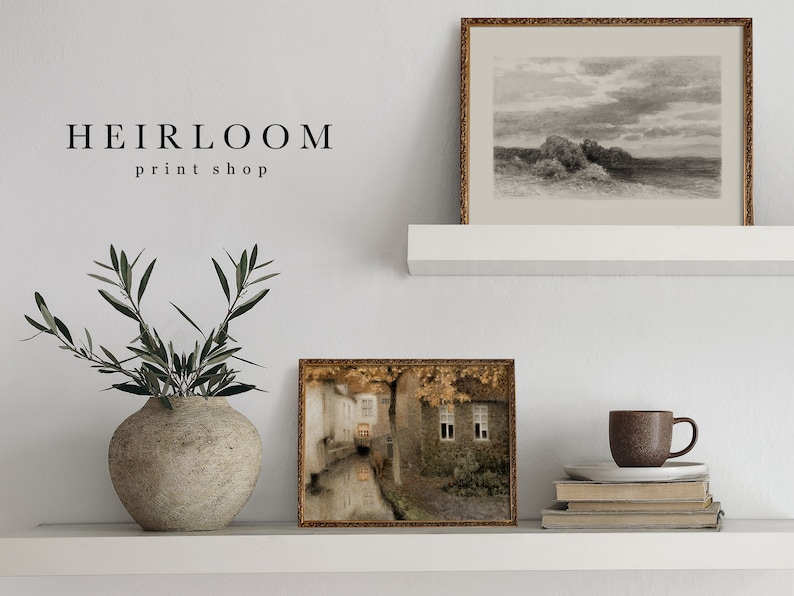 May include: A display of framed art prints and decorative items on a white shelf. The prints include a landscape sketch and a street scene. A ceramic vase holds olive branches. The text "HEIRLOOM print shop" is visible.