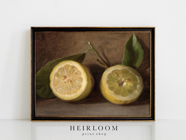 May include: A framed still life painting featuring two lemon halves with green leaves. The lemons are yellow with visible pulp, set against a dark brown background. The frame is black with gold trim. The text "HEIRLOOM print shop" is at the bottom.