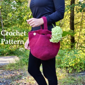 Könnte beinhalten: Burgunderfarbene Häkeltasche mit Henkel und Zierknopf. Die Tasche enthält eine grüne Blume und wird von einer Person getragen, die ein schwarzes Langarmshirt und eine schwarze Hose trägt. Die Worte "Crochet Pattern" sind sichtbar.