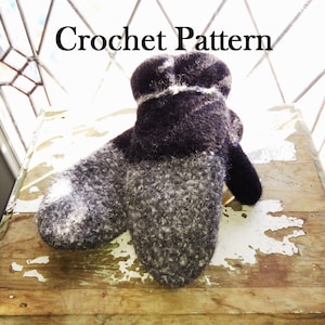 Pode incluir: Um close-up de uma luva de crochet preta e cinza com uma faixa branca. A luva está sobre uma superfície de madeira.