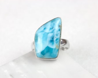 May include: A silver ring with a large, light blue, irregularly shaped gemstone. The gemstone has a cloudy, marbled appearance. D. US SZ 7.5