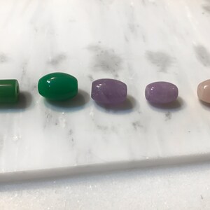 May include: Five oval-shaped gemstone beads. Two green jade beads, one purple amethyst bead, and two pink rose quartz beads.